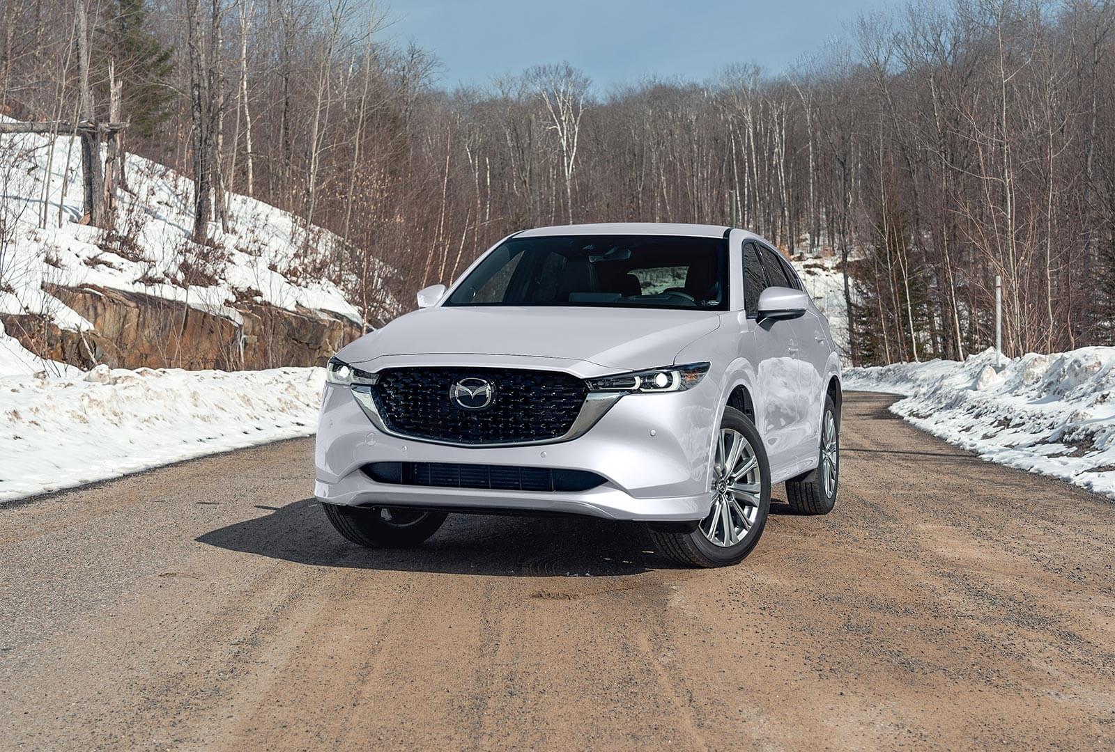 Vue avant d’un CX-5 blanc rhodium métallisé garé sur une route enneigée. 