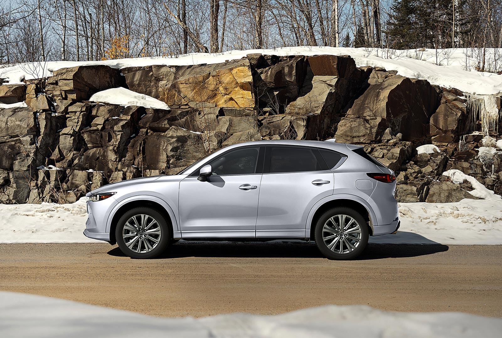 CX-5 parked in front of rock wall on snowy country road.