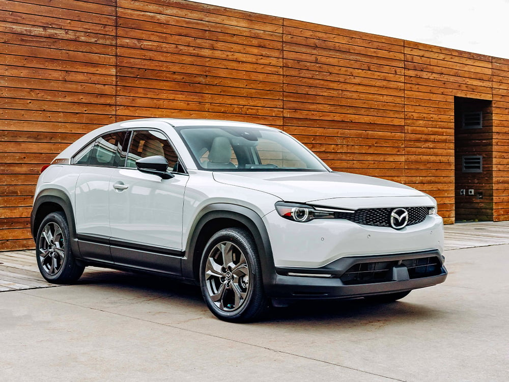 Mazda MX-30 blanc arctique garé devant un mur de lattes en bois