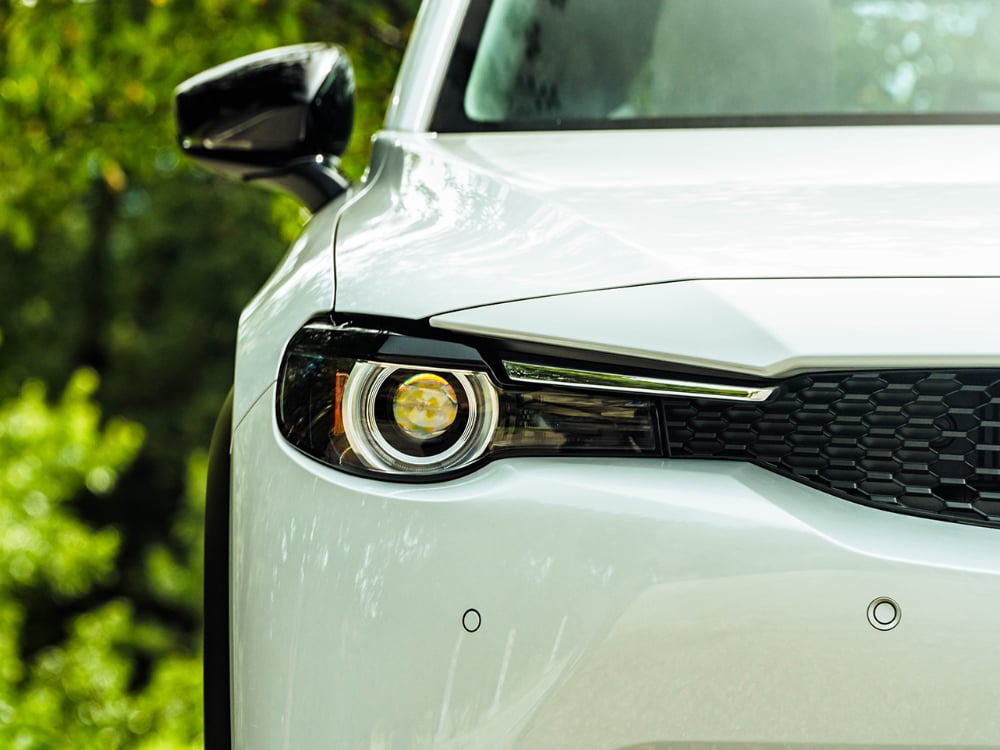 Closeup of front right Arctic White MX-30 headlight in daylight.