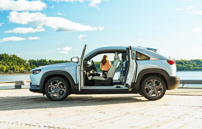 MX-30 EV’s open freestyle doors frame a woman standing on a pier looking out at the water.