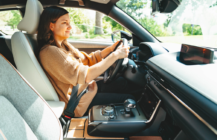 Driver in MX-30 EV smiles, comfortable situated with seatbelt on.