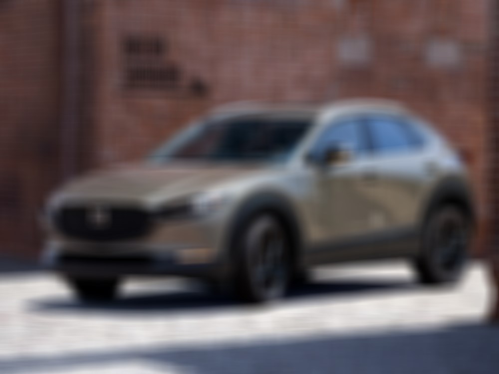 Zircon San Metallic CX-30 parked on cobblestone road behind red brick building.  