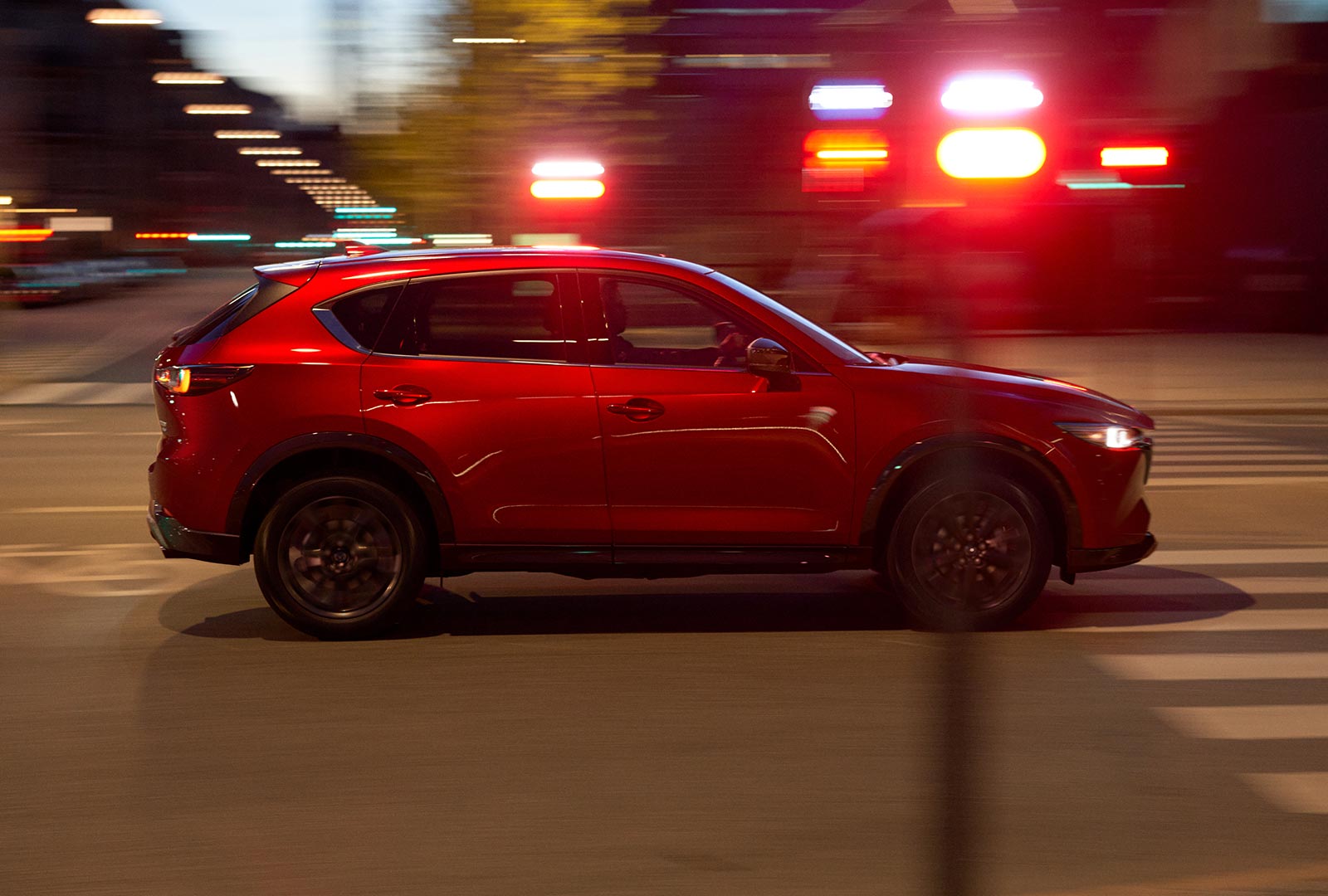 Profil flou d’un CX-5 rouge vibrant cristal métallisé qui se déplace dans une rue. 