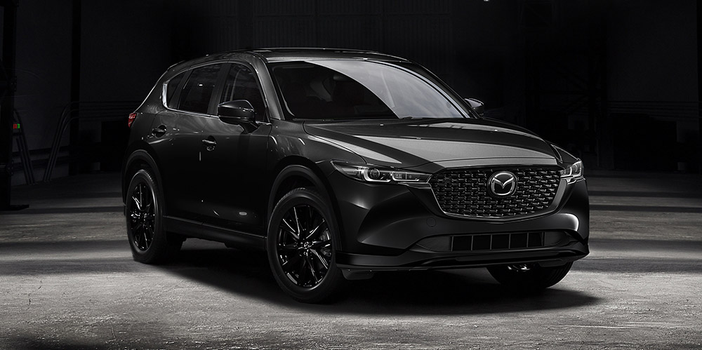 Un CX-5 noir de jais mica sur le plancher de béton d’un entrepôt reflétant l’éclairage intense qui le surplombe. 