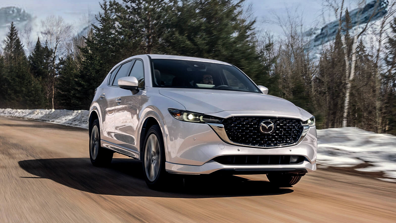 Un CX-5 blanc rhodium métallisé sur une route de campagne hivernale.  