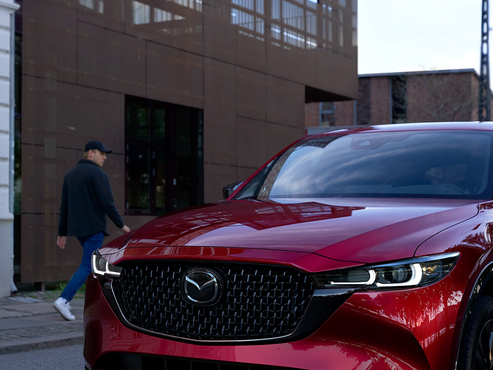 Soul Red Crystal Metallic Mazda CX-5 with Sport Design trim approaches on urban street. 