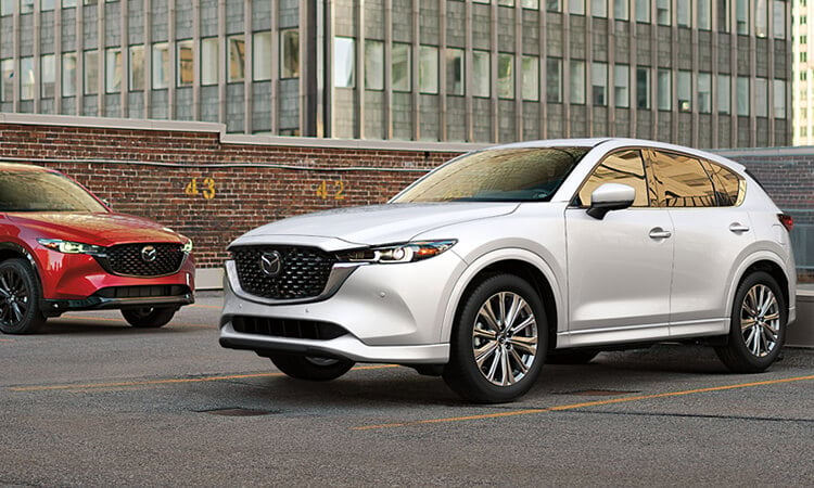 Un CX-5 blanc rhodium métallisé et un CX-5 rouge vibrant cristal métallisé garés au dernier étage d’un stationnement, à la lumière du jour. 