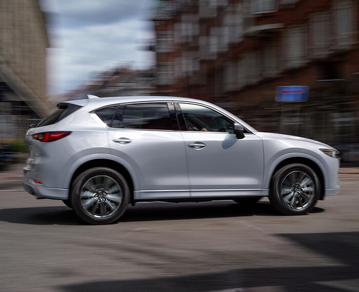 CX-5 driving through city’s main street intersection on a sunny day.