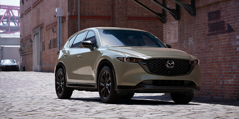 Zircon Sand Metallic CX-5 parked on cobblestone alley behind red brick buildings in day light.