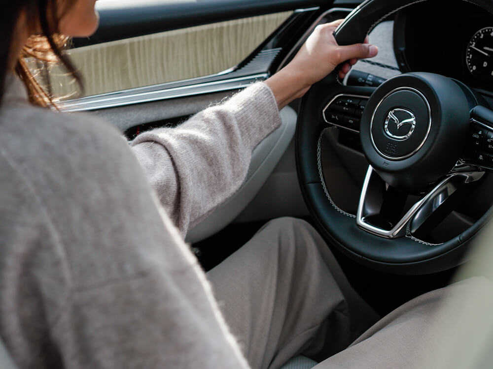 Un conducteur vêtu d’un chandail de laine, les mains sur le volant, à l’intérieur d’un CX-90.   