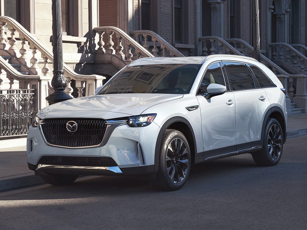 Arctic White CX-90 Parked along city street lined with regal concrete apartment stairs. 