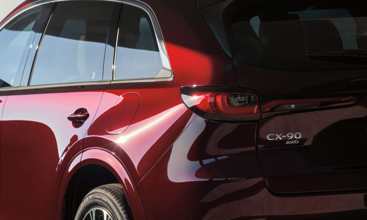 Sunlight gleaming off of the back left wheel well and taillight of an Artisan Red CX-90.