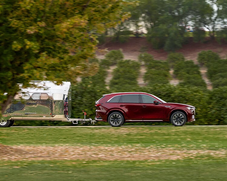 Un VÉHR CX-90 rouge artisan tracte une remorque de camping sur une route de campagne verdoyante.  