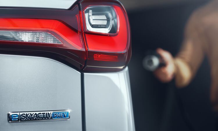 Un conducteur s’approche d’une Mazda avec un chargeur de niveau 2 à la main. 