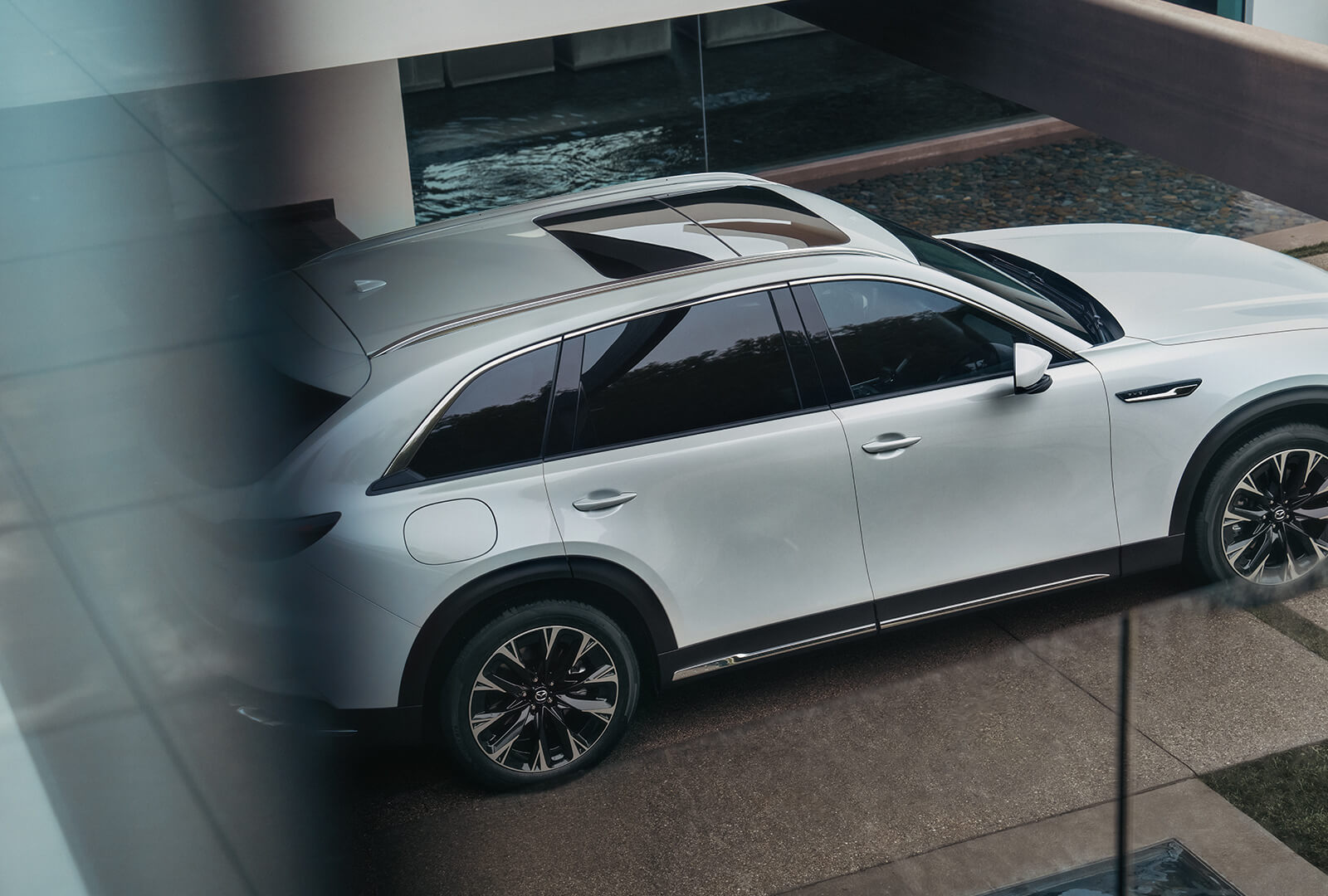 View from above and Arctic White CX-90 parked next to a water feature. 