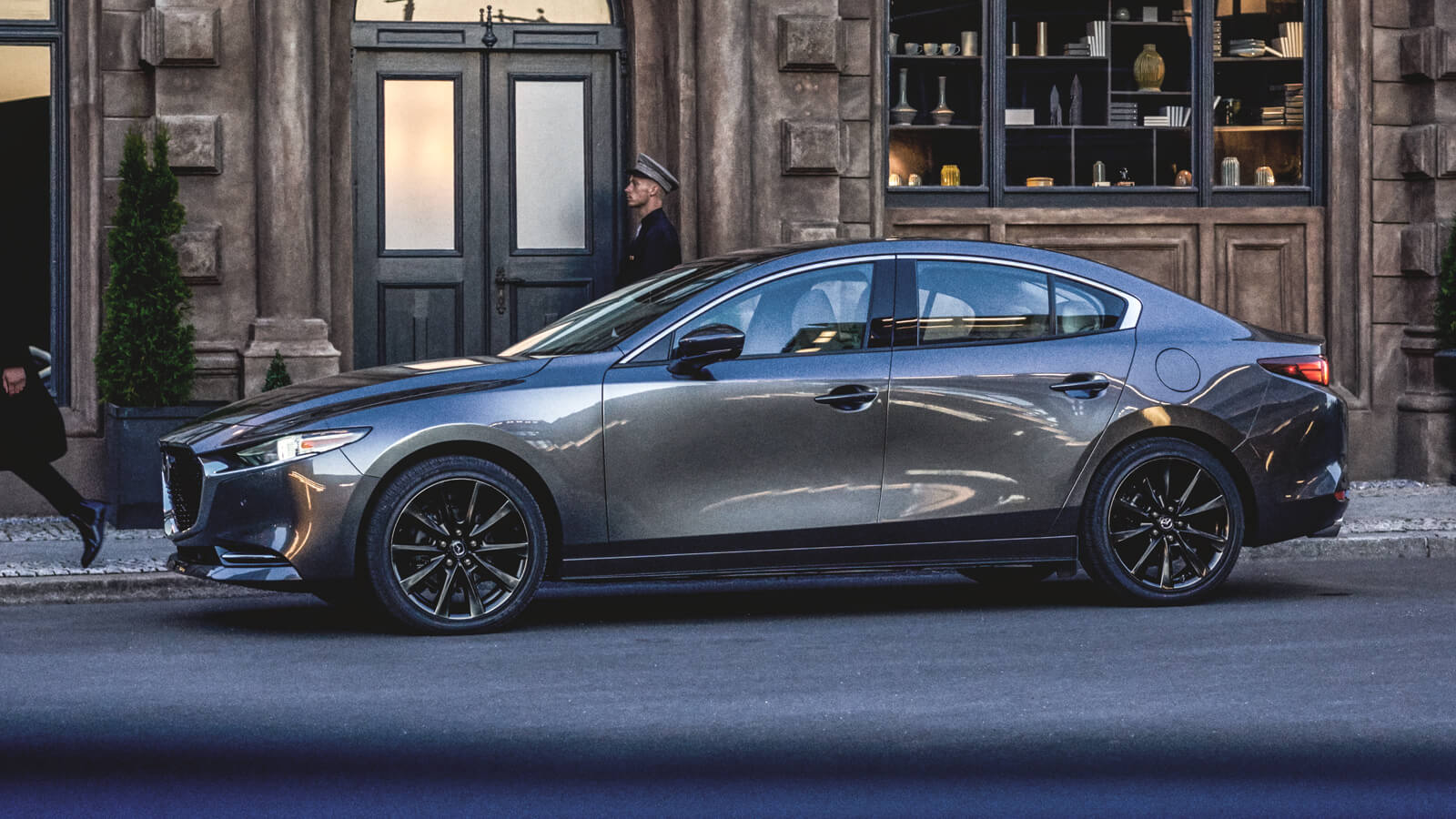 Une berline Mazda3 garée devant l’entrée d’un magasin dans une rue urbaine. 