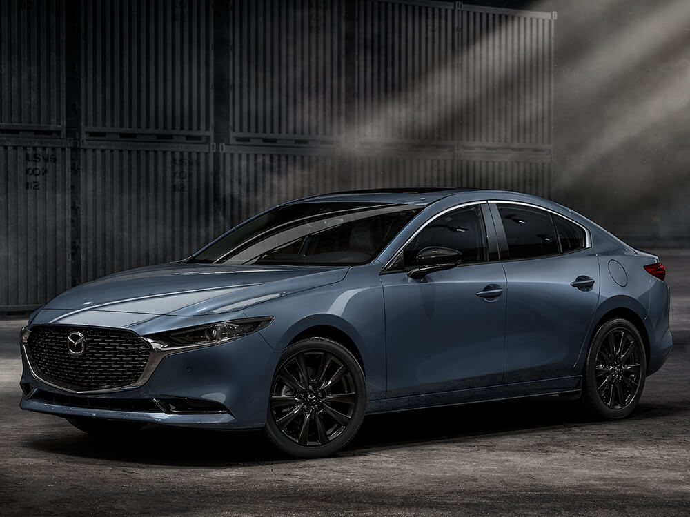 Une rutilante Mazda3 garée dans un hangar d’entreposage de conteneurs, la lumière traverse la poussière dans l’air. 