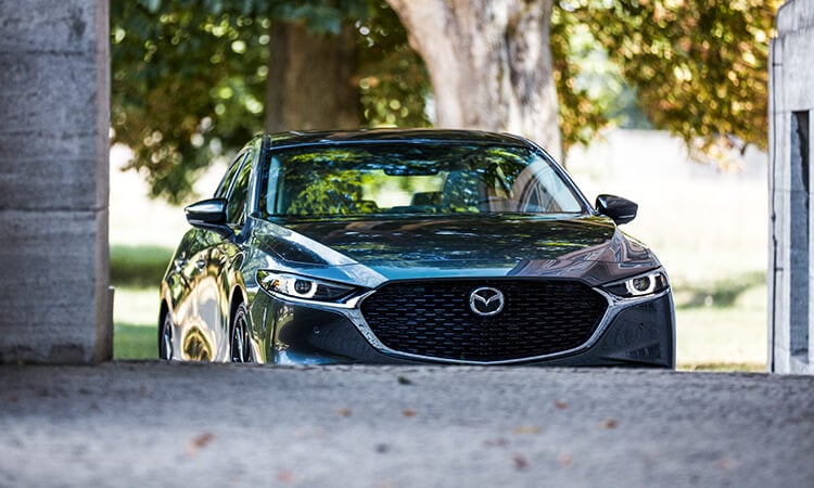 Front of the Mazda3 sedan approaching an inclined driveway.  