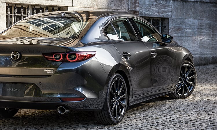 Une berline Mazda3 les roues tournées pour sortir d’une ruelle pavée en plein jour. 