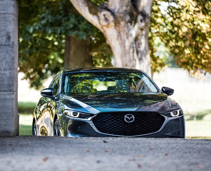 Front of the Mazda3 sedan approaching an inclined driveway.  