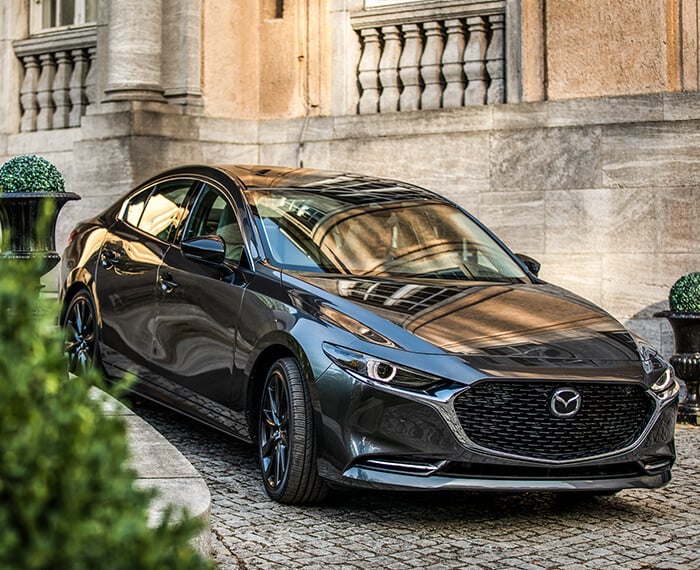 Mazda3 sedan making a tight left turn down a steep cobble stone pathway.