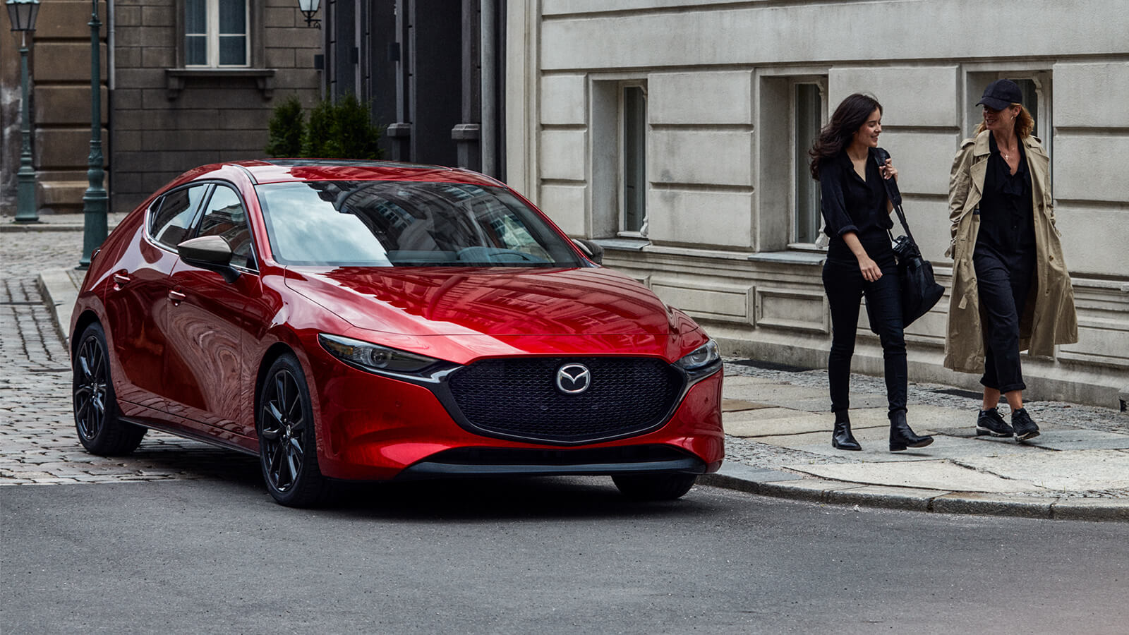 Soul Red Crystal Metallic Mazda3 Sport parked at the corner of a cobblestone side street and paved road.