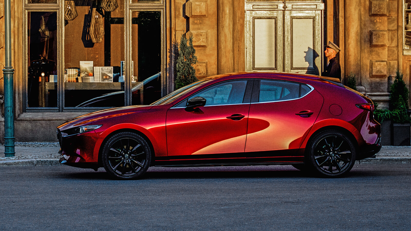 Soul Red Crystal Metallic Mazda3 Sport parked in front of main street shop at sundown.  