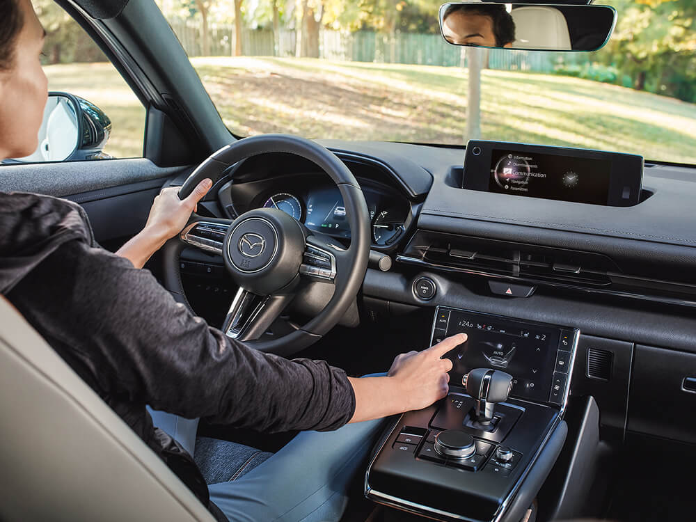 Gros plan depuis la banquette arrière d’un MX-30 montrant le conducteur qui appuie sur l’écran couleur tactile de la console centrale.