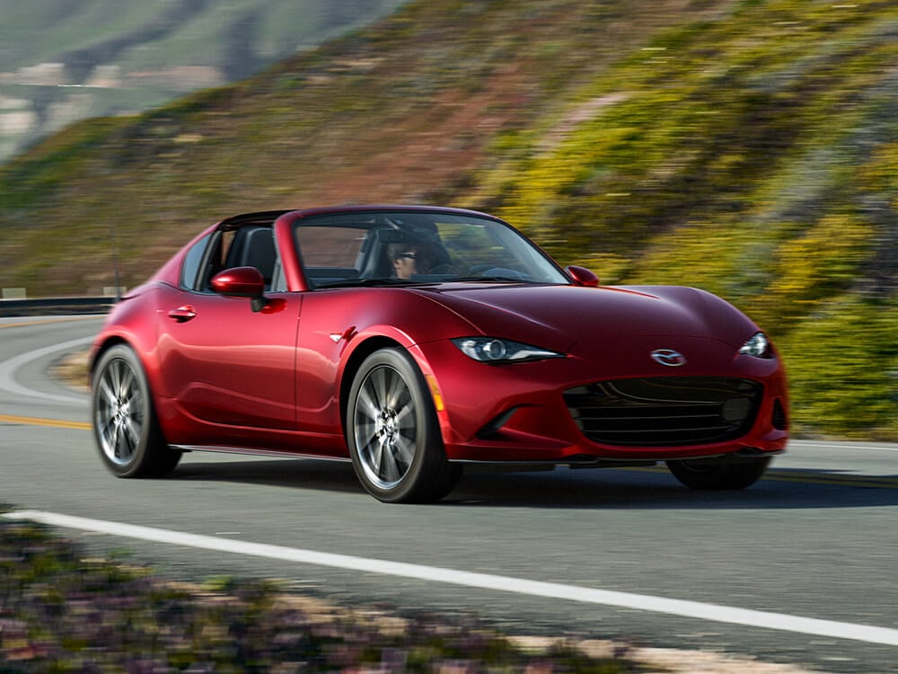 Une MX-5 RF rouge vibrant cristal métallisé prend un virage sur une route verdoyante escarpée.