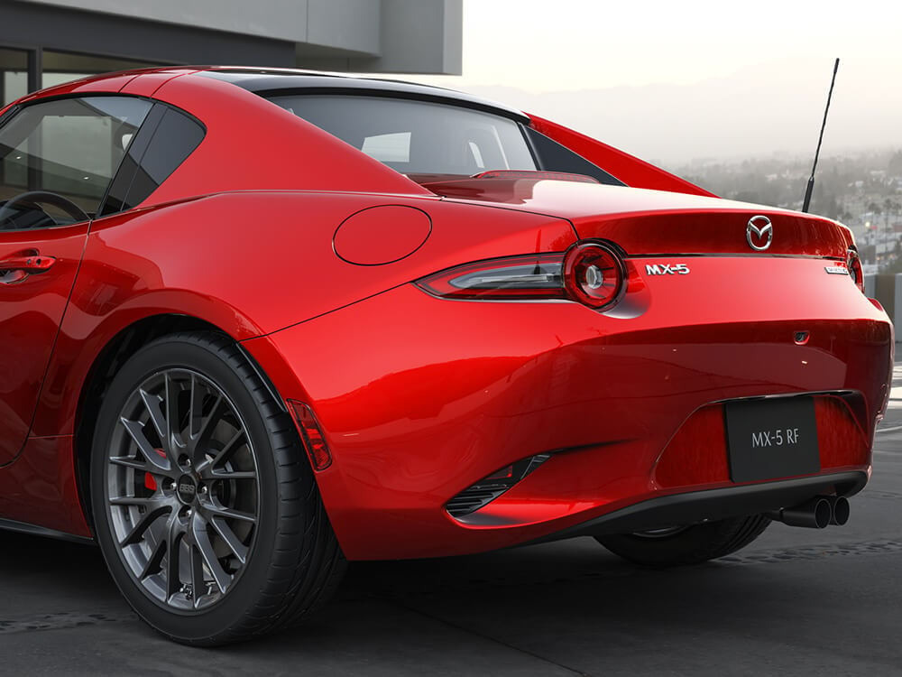 Close up on left taillight on Mazda MX-5 ST GS-P Sport Package with Soul Red Crystal finish, reflecting the green hills behind.