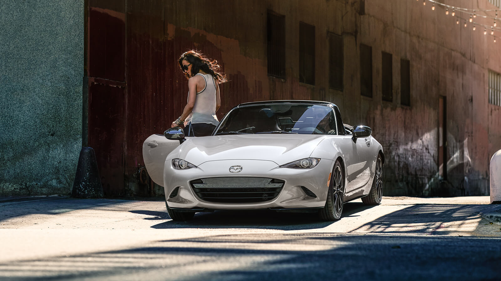 Une femme sort d’une MX-5 blanc neige nacré stationnée devant une porte en bois patiné.