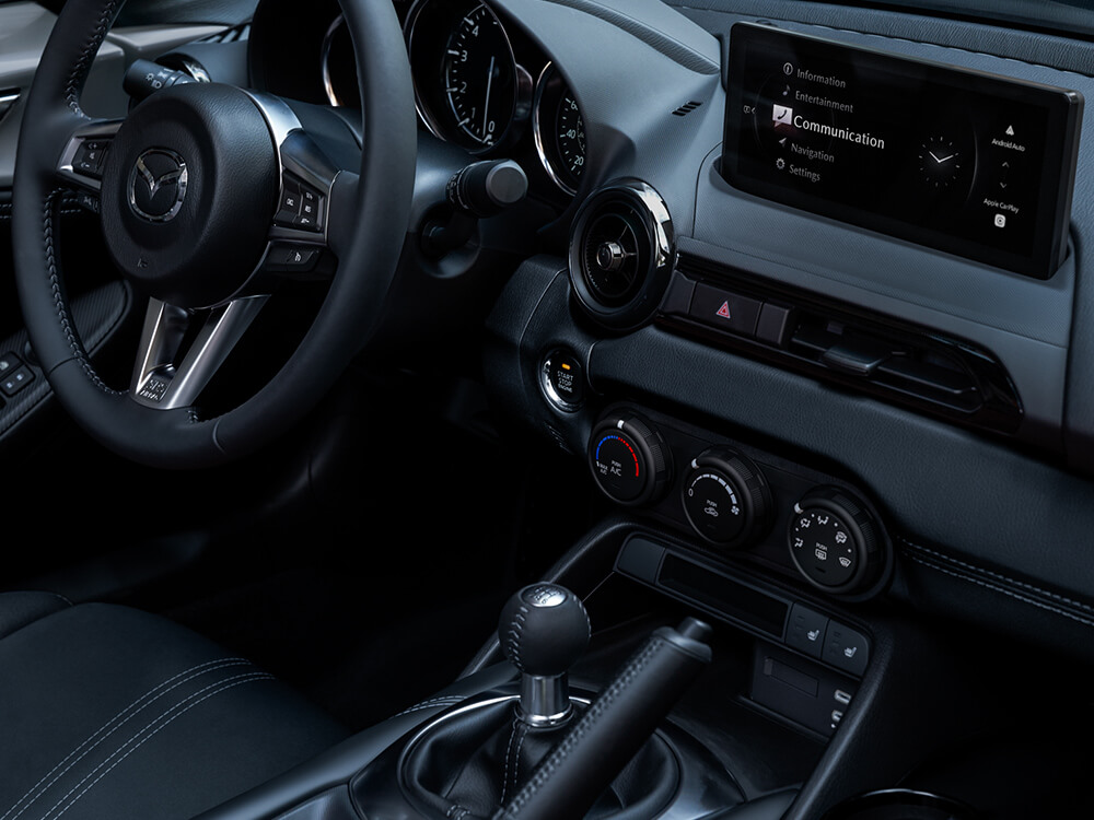 Vue de l’intérieur d’une MX-5 ST côté passager montrant l’interface humain-machine autour de la console centrale, du volant et de l’écran tactile.