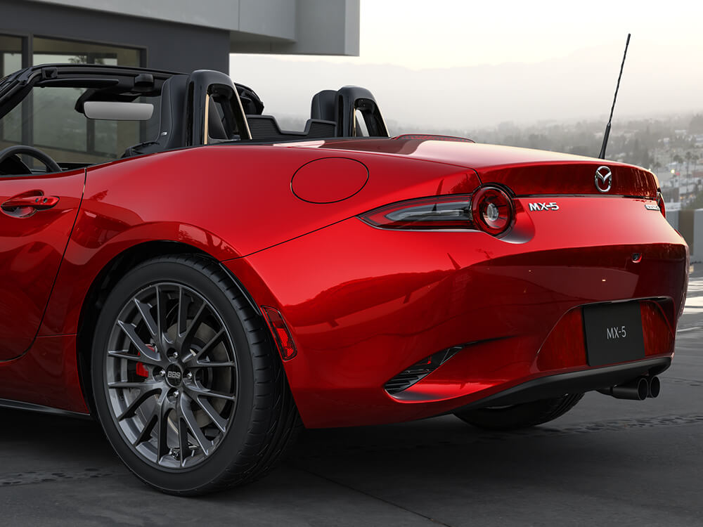 Gros plan sur le feu arrière gauche d’une Mazda MX-5 ST GS-P avec Groupe sport rouge vibrant cristal reflétant les collines verdoyantes derrière. 