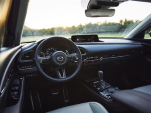 Driver’s seat view of CX-30 at dusk, highlighting steering wheel, dash, console, and door controls.