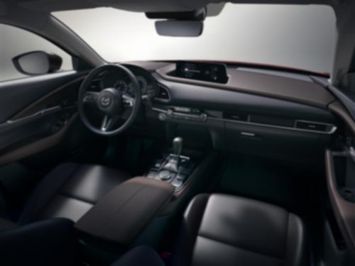 In seamless studio environment, view from CX-30 passenger’s side inside back, looking forward and down at the front seats, steering, dash, console and display.