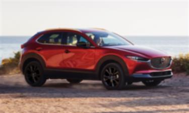 Un Mazda CX-30 rouge vibrant cristal métallisé garé sur un chemin de terre surplombant un grand lac en arrière-plan. 