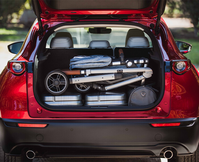 Le hayon ouvert d’un CX-30 révêle un grand espace de chargement contenant un sac à dos, une poussette pliable, deux grandes glacières et un sac de sport. 