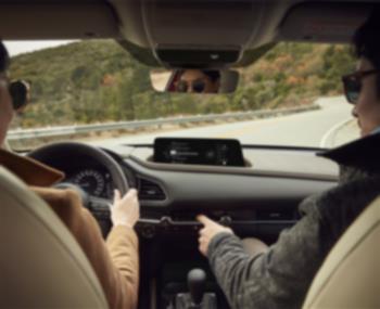 Vue de l’extérieur, côté conducteur, on voit le conducteur qui tient le volant à l’intérieur du CX-30.