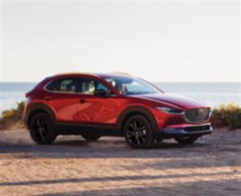 Soul Red Crystal Metallic Mazda CX-30 drives along mountainous highway. 