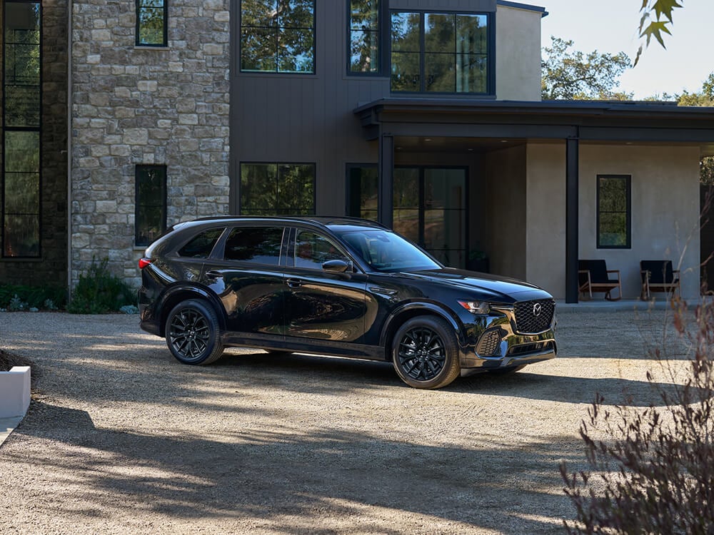 Un CX-70 noir de jais mica garé dans une grande allée dégagée devant une maison rurale.