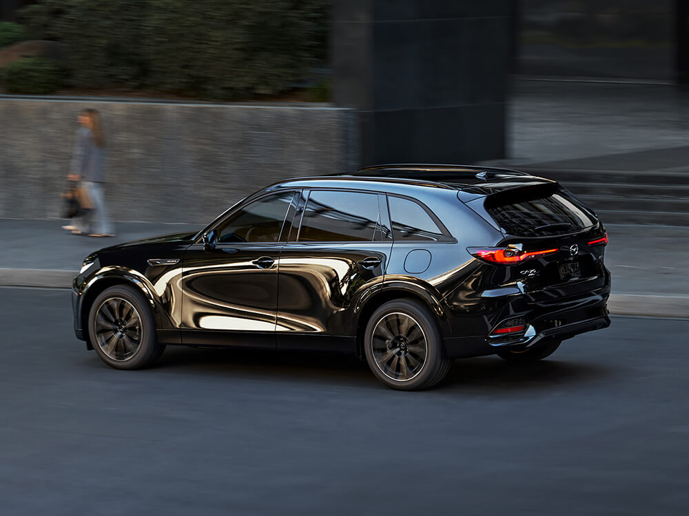 Jet Black Mica CX-70 driving down city street, the city’s reflection on the driver’s side door gives it a unique look.