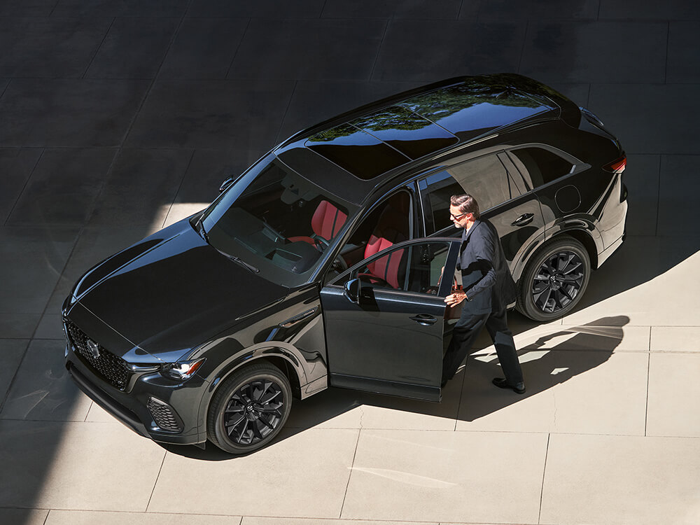 Shot from above, a man enters a Jet Black Mica CX-70, the sunlight reveals the Garnet Red Leather interior seats.