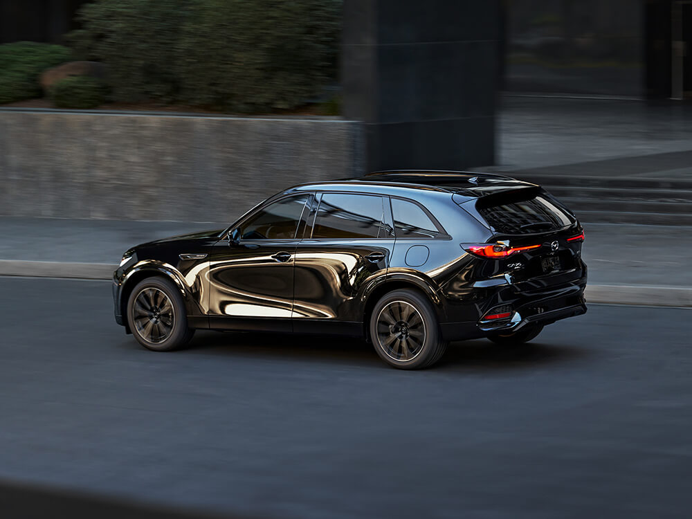 Jet Black Mica CX-70 driving down city street, the city’s reflection on the driver’s side door gives it a unique look.