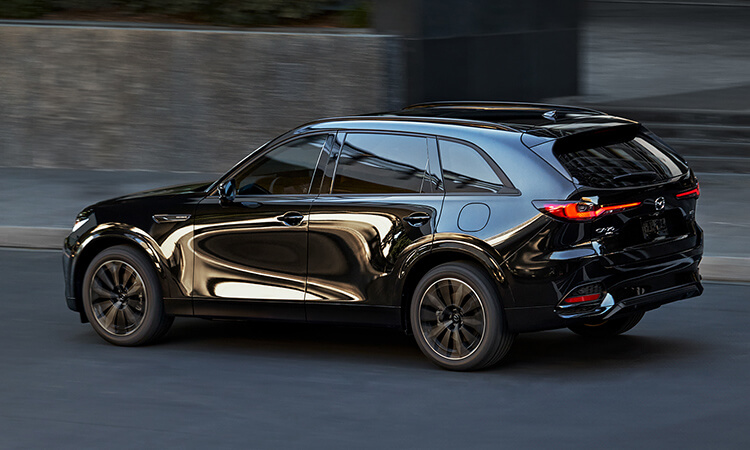 Un CX-70 noir de jais mica dans une rue urbaine; le reflet de la ville sur la porte côté conducteur lui donne un look unique.