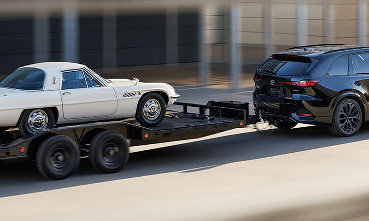 Un CX-70 noir de jais mica tractant une remorque transportant un véhicule récréatif classique Mazda blanc.