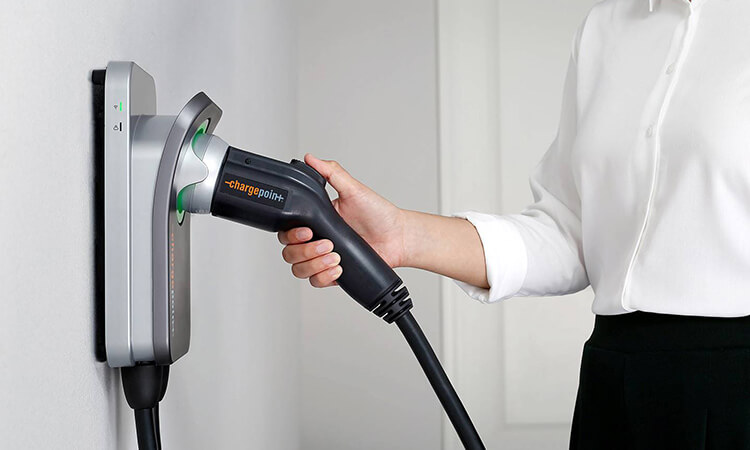 A hand grabs a professionally installed level 2 charger from the wall in a garage.