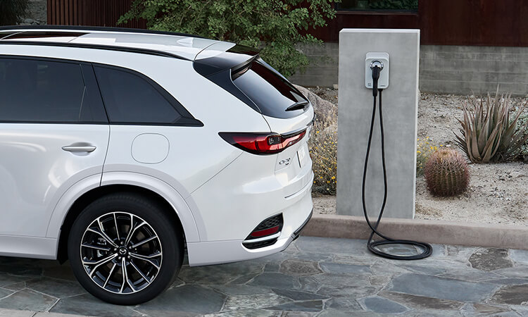 The rear of a Rhodium White Metallic CX-70 parked in front of level 2 charger.