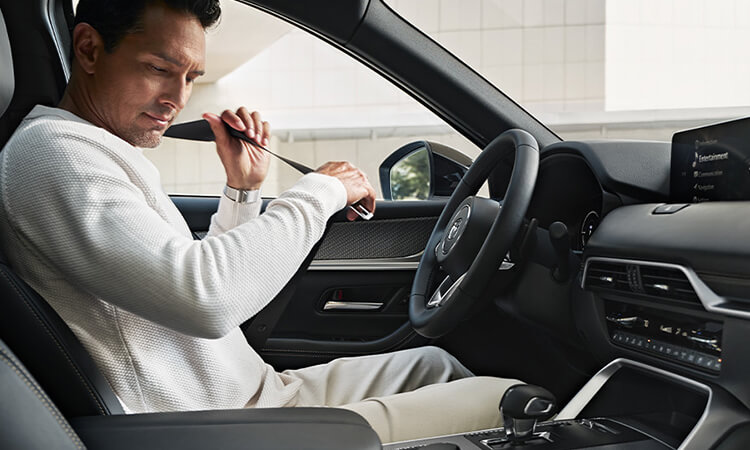 Man buckles his seatbelt in the driver’s seat of a parked CX-70.