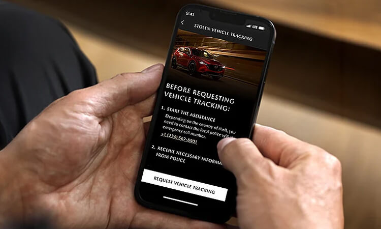 Des mains tiennent un téléphone intelligent affichant le suivi de véhicule volé de Mazda à l’écran. 